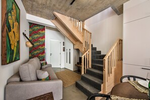 A staircase with wooden steps and a handrail, a grey sofa with cushions, and a colorful abstract painting on the wall.