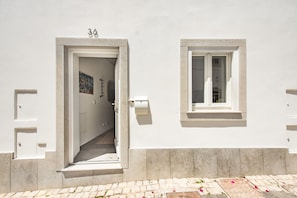 A white building with a door and window, a number '36' above the door, and a small window on the right side. - Cozy Mozambican Retreat (Cabanas de tavira)