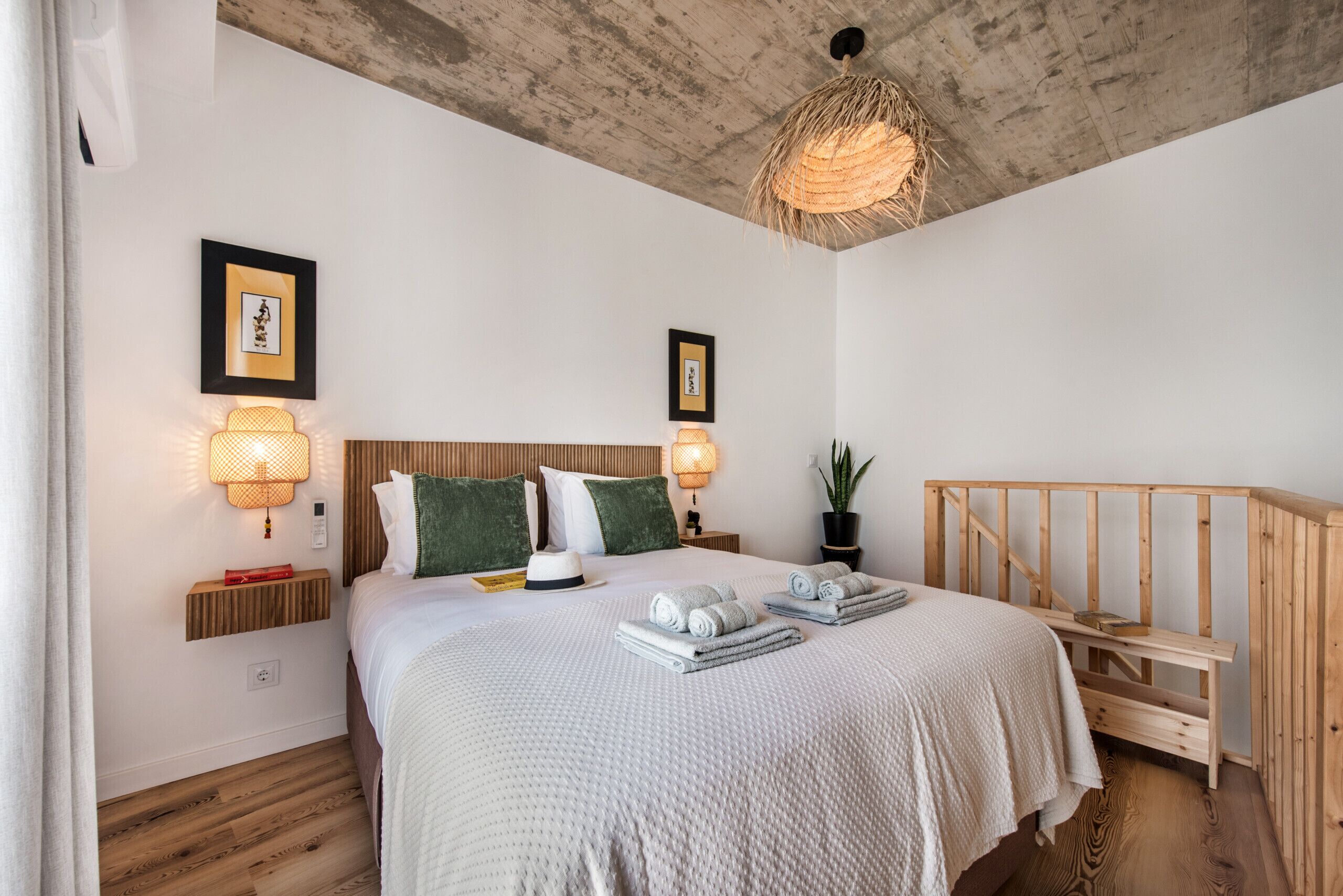 A bedroom with a wooden headboard, two wall-mounted lamps, a bed with a white quilt, and a wooden staircase.