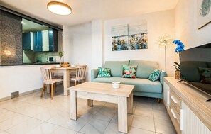 Ein modernes Wohnzimmer mit einer Couch, einem Esstisch, Stühlen, einem Couchtisch, einem Fernseher und einer Küchenzeile mit Schränken und einer Mikrowelle.