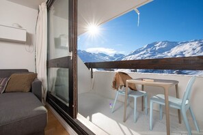 Un balcon avec vue sur des montagnes enneigées, un canapé gris et une table avec des chaises.