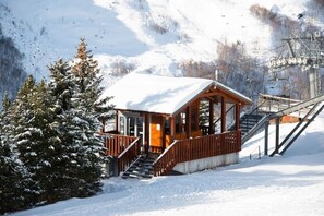 Une cabane en bois, dont le toit est recouvert de neige, avec un escalier en bois et une vue sur une montagne enneigée.