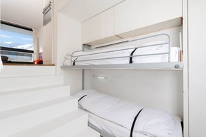 A bunk bed room with white bedding, a window with a view of snow-capped mountains, and a staircase.