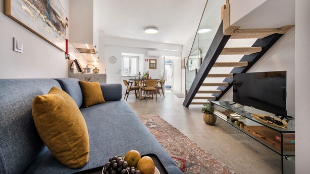 A modern living room with a sofa, a glass coffee table with fruit, a television, and a staircase.