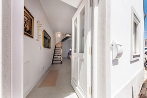 Un couloir avec un escalier, une porte et un luminaire fixé au mur.