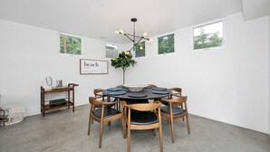 Een eetgedeelte met een ronde tafel, zes houten stoelen, een hanglamp en een lijst met een woordkunstwerk aan de muur.
