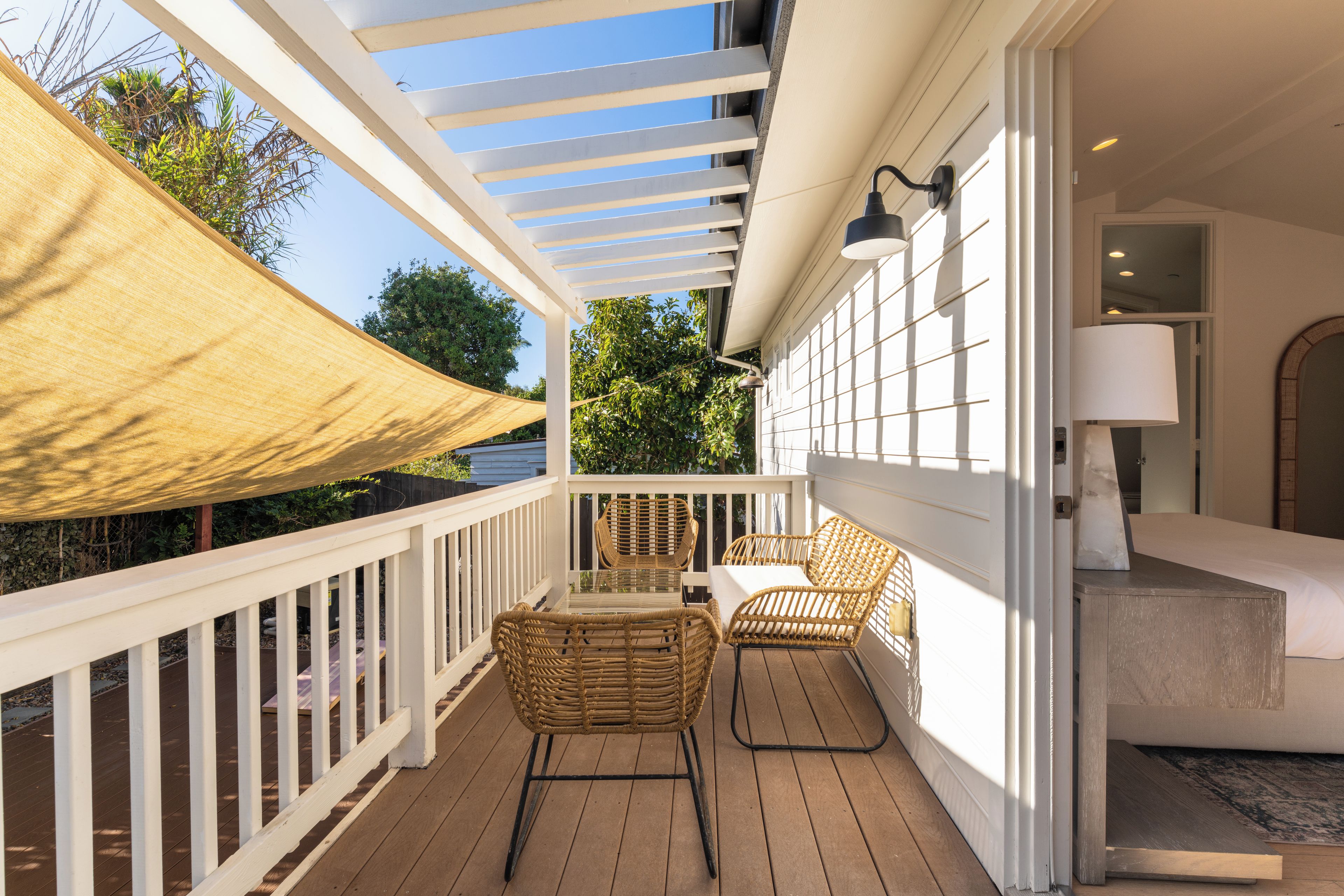 A covered outdoor balcony with wicker furniture, a table, and a lamp.