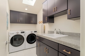 A modern kitchen with dark cabinets, a built-in washing machine, and a granite countertop. - Family Beach House w/ Pool & AC + Walking Distance to Shops + Food (Encinitas)