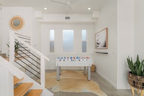 A modern interior with a staircase, a foosball table, and a large plant. - Family Beach House w/ Pool & AC + Walking Distance to Shops + Food (Encinitas)