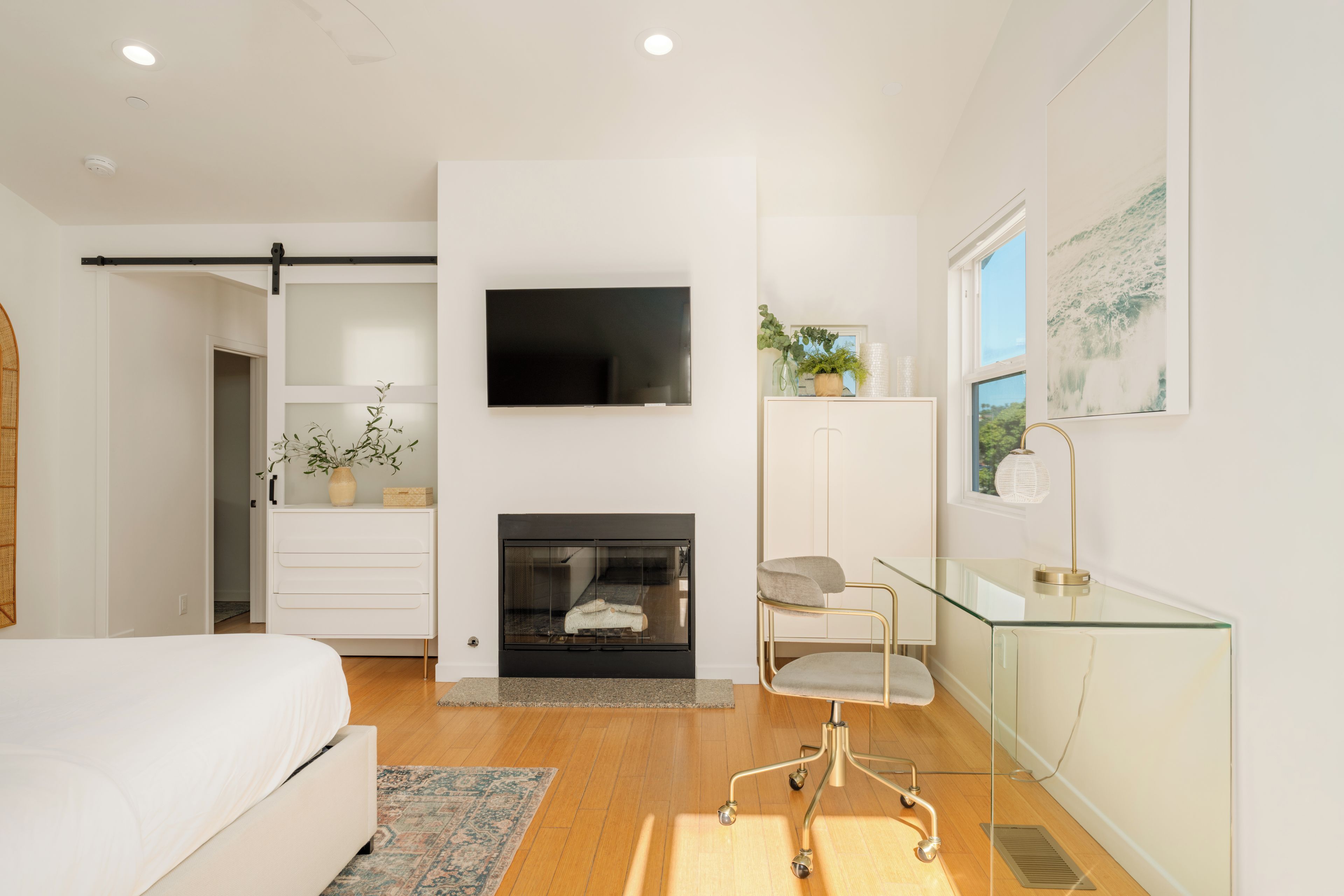 A modern bedroom with a bed, a TV, a fireplace, a desk, and a window with a view.