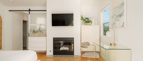 A modern bedroom with a bed, a TV, a fireplace, a desk, and a window with a view.