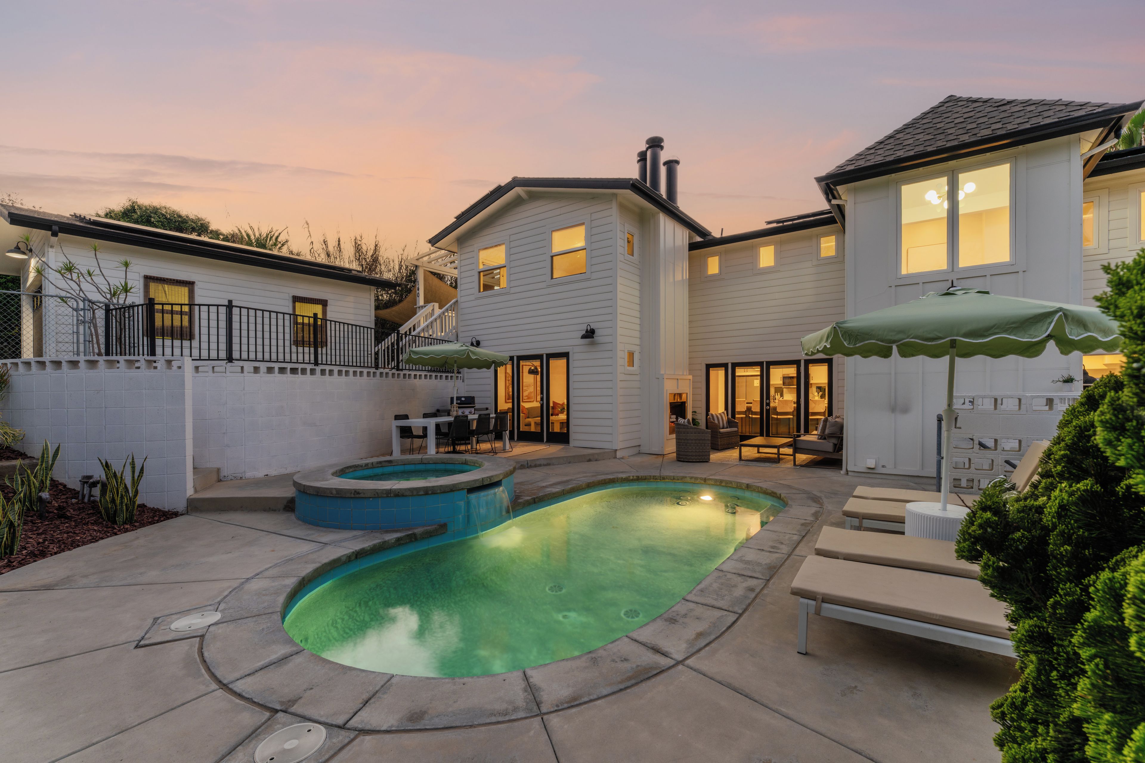 Un jardin à l’arrière d’une maison d’habitation, avec une piscine, un espace patio aménagé avec du mobilier d’extérieur, et une maison dotée de nombreuses fenêtres.