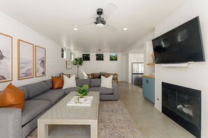 A modern living room with a grey sofa, a coffee table, and a flat-screen TV mounted on the wall. - Family Beach House w/ Pool & AC + Walking Distance to Shops + Food (Encinitas)