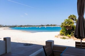 Blick auf einen Strand mit einer Terrassenanlage, inklusive Tisch, Stühlen und Sonnenschirm.