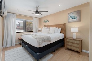 Une chambre à coucher avec un lit, des tables de chevet, un ventilateur de plafond et une fenêtre avec des rideaux.