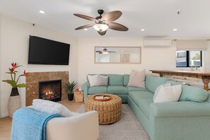 Ein Wohnzimmer mit Kamin, einem grünen Sofa, einem Deckenventilator und einem Flachbildfernseher.