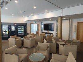 Vestíbulo de hotel con asientos, televisor, máquinas expendedoras y un pilar.