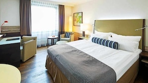 Habitación de hotel con una cama grande, un escritorio, una silla, una mesita y una ventana con cortinas.