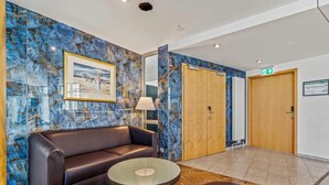 Un vestíbulo con un sofá de cuero, una mesa con cubierta de vidrio y un banco. Hay dos puertas de madera y un cuadro en la pared.