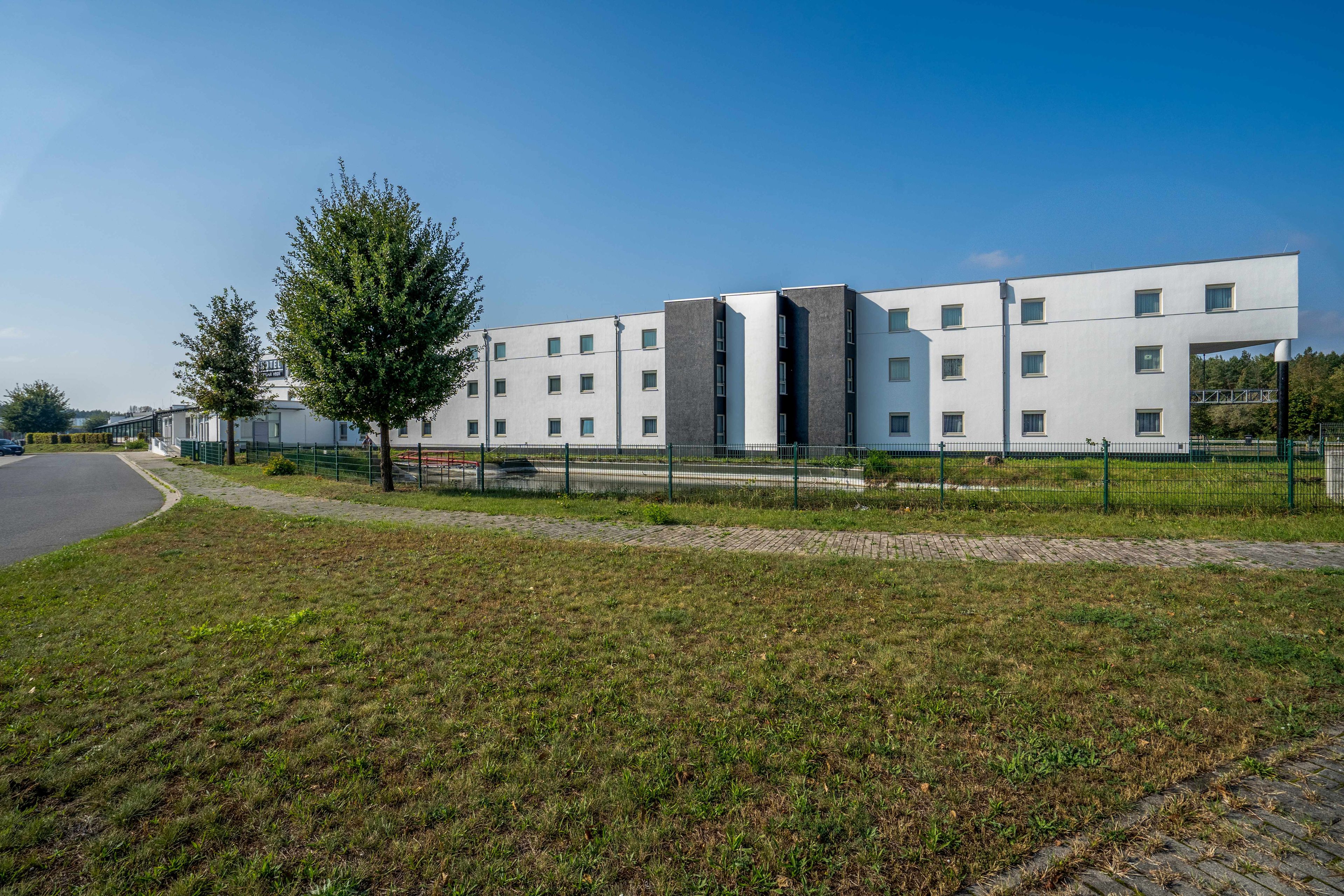 Ein modernes Hotel mit flacher Fassade, zahlreichen Fenstern und einem gepflasterten Zugangsbereich.