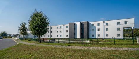 A modern hotel with a flat facade, multiple windows, and a paved driveway.