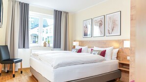 Hotellihuone, jossa on suuri sänky, tuoli, ikkuna, jossa on verhot, ja seinälle kiinnitetty taideteos.