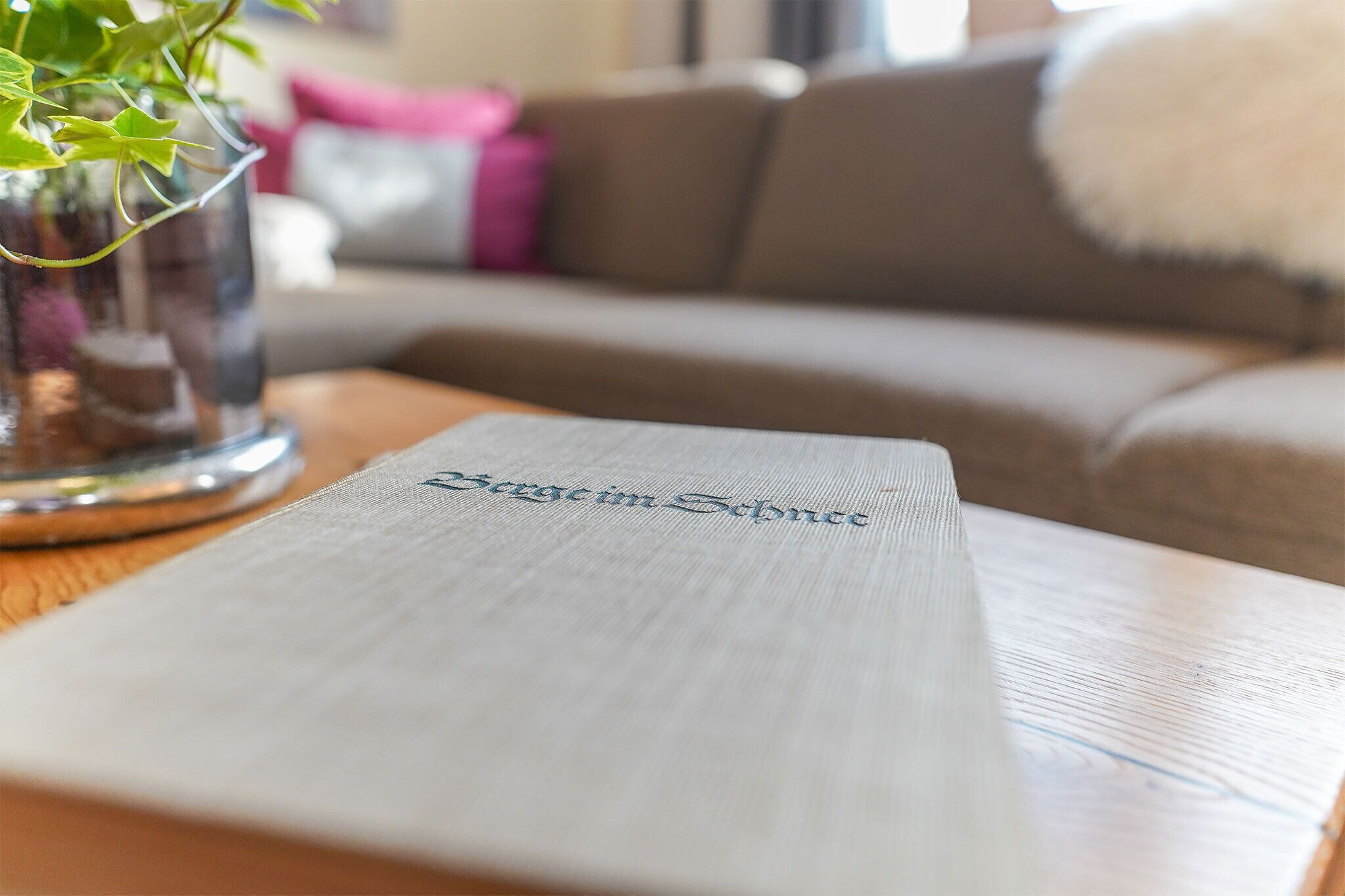 A book titled 'Sergio Scuderi' on a wooden table with a blurred background of a couch and a vase with green leaves.