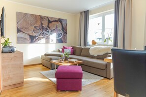 A living room with a sofa, ottoman, coffee table, and a painting on the wall.