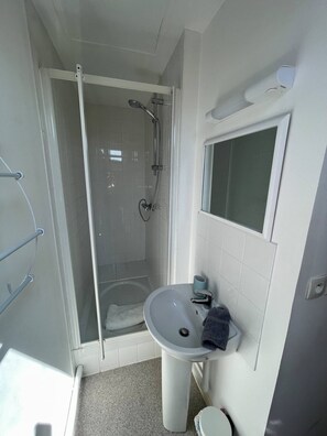 Een badkamer met een douchecabine van glas, een wastafel en een spiegel.
