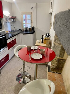 Een kleine keuken met een eethoek, bestaande uit een rode tafel, witte stoelen en een spoelbak.
