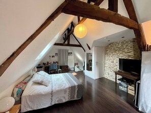 Une chambre à coucher aménagée dans un espace mansardé, avec un plafond en pente, un lit, un bureau, une télévision et un mur en pierre.