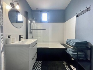 Un baño moderno con lavamanos, espejo y zona de ducha blancos.