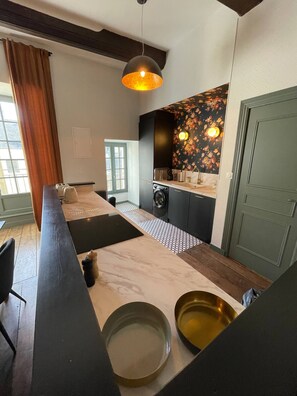 A modern kitchen with a central island, a washing machine, and a dining area with a table and chairs. - AppartCosy 08 5pers charm and authenticity (Vitré)