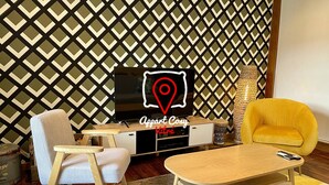 Una sala de estar moderna con una televisión, un sillón amarillo, una mesa de centro de madera y una pared con estampado.