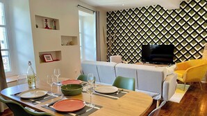 Un comedor con una mesa de madera, platos verdes y naranjas, y cristalería transparente.