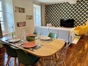A dining area with a wooden table, green and orange plates, and clear glassware. - EasyHome 19 Duplex  in a quiet location (Vitré)