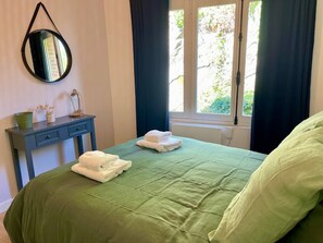 A bedroom with a bed, a nightstand, a mirror, and a window with curtains.
