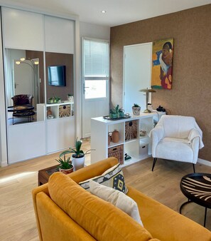 Ein modernes Wohnzimmer mit einer Couch, einem Sessel, einem Fernseher und einem Gemälde an der Wand.