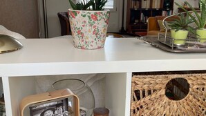 A white shelf with a potted plant, a framed photo, a wooden sculpture, and a woven basket.