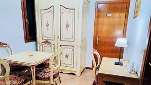 A dining area with a table and chairs, a cabinet, a door marked 'TOILETTE', and a lamp on a desk. - Room-venezia Baroque Charm (Venice)