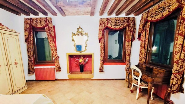 A room with a wooden ceiling, a mirror, a fireplace, a wooden cabinet, and a chair. - Room-venezia Baroque Charm (Venice)