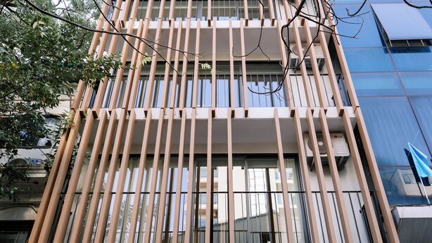 Un bâtiment moderne doté de lambris en bois verticaux, de grandes fenêtres et d’une façade en verre réfléchissant.