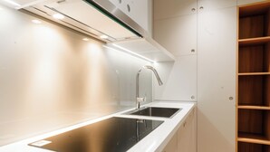 Une cuisine moderne dotée d’une plaque de cuisson à induction noire, d’un robinet en acier inoxydable et de meubles blancs.