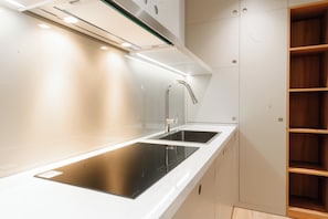 Una cocina moderna con placa de inducción negra, grifo de acero inoxidable y armarios blancos.