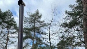 Una sauna de madera con una chimenea, una escalera de madera y una barandilla de metal.