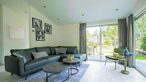 Una sala de estar moderna con un sofá, una mesa de centro y vistas a un área exterior a través de grandes puertas correderas.
