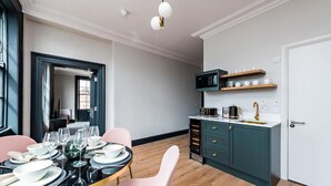 A modern dining area with a round table set for four, a kitchen with teal cabinetry, and a white door. - One Capel Suites (Dublin)