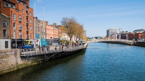 A riverside walkway with buildings, a bridge, and a clear sky. - One Capel Suites (Dublin)