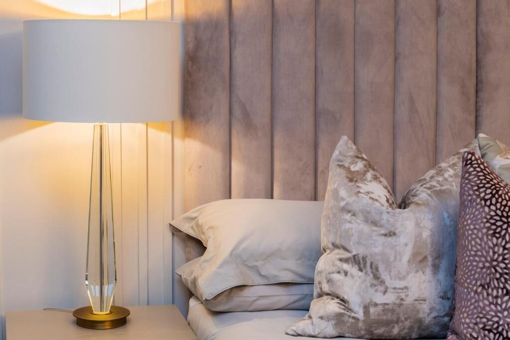 Una cama con almohadas, una lámpara de noche y un cabecero de madera.