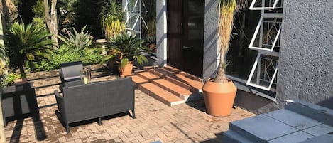 A patio area with a pergola, outdoor seating, potted plants, and a view of a building with large windows.